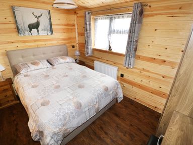 A bedroom with a double bed two bedside tables curtains over the window and a painting of a stag on the wooden wall at Hayfields in Grimston