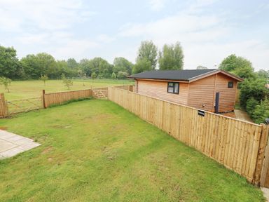 A fenced yard with grass and a wooden shed next to a wooden fence at Hayfields in Grimston