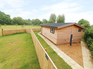 A wooden cabin with a fenced grassy yard and paved pathways at Hayfields in Grimston