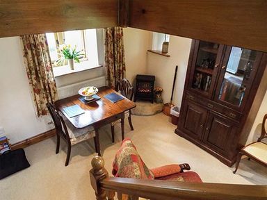 A dining area with a wooden table and chairs next to a window with floral curtains and a cabinet at The Old Cider House in Prestbury near Cheltenham
