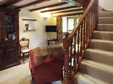 A living room with wooden staircase a cabinet a chair and a television at The Old Cider House Prestbury near Cheltenham