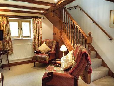 A sitting area with two armchairs and a small table under wooden stairs at The Old Cider House Prestbury near Cheltenham