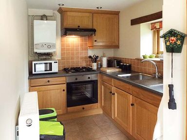 A kitchen with wooden cabinets a gas stove an oven a microwave a sink and kitchen utensils at The Old Cider House in Prestbury near Cheltenham