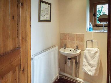 A small bathroom with a wall-mounted sink a towel hanging on a rack a radiator a framed picture on the wall and a window with a soap dispenser and a mirror at The Old Cider House in Prestbury near Cheltenham