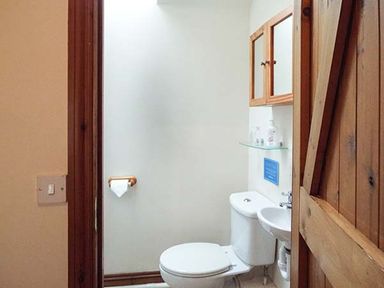 A small bathroom with a toilet and a sink with wooden cabinet above at The Old Cider House Prestbury near Cheltenham