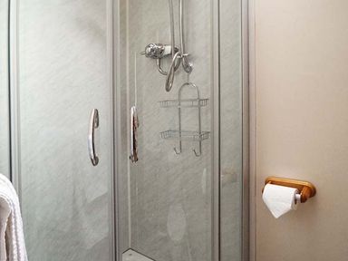 A shower cubicle with glass doors and chrome handles a metal shower caddy and a toilet paper holder on the wall at The Old Cider House in Prestbury near Cheltenham