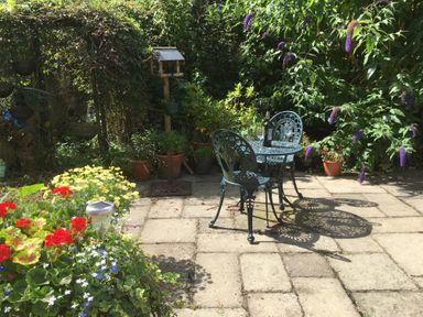 A garden patio with a metal table and two chairs and plants in pots with flowers at The Old Cider House in Prestbury near Cheltenham