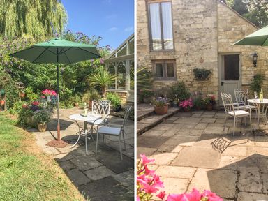 An outdoor patio area with metal chairs and tables under a green umbrella surrounded by plants and flowers at The Old Cider House in Prestbury near Cheltenham