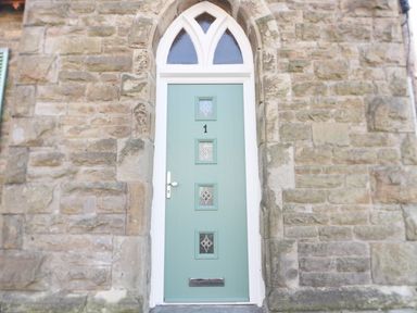 A stone wall with a green door featuring four glass panels and a metal mail slot at No 1 Church Cottages Llanelli