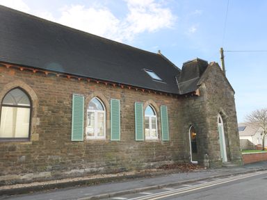 A stone building with arched windows and blue shutters on a street at No 1 Church Cottages in Llanelli