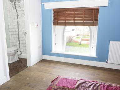 A bedroom with blue walls wooden floor and an arched window with wooden blinds at No 1 Church Cottages Llanelli
