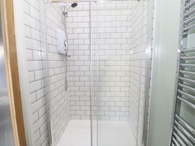 A shower area with white subway tiled walls and glass doors at No 1 Church Cottages in Llanelli
