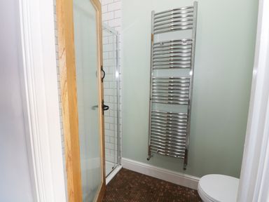 A bathroom with a glass shower enclosure a chrome towel radiator and a toilet at No 1 Church Cottages in Llanelli