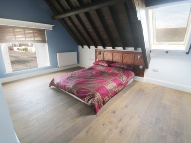 A bedroom with a double bed under a sloped ceiling with a window and a radiator at No 1 Church Cottages in Llanelli