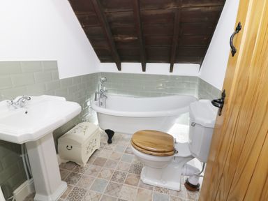 A bathroom with a pedestal sink toilet with wooden seat and clawfoot bathtub under a wooden sloped ceiling at No 1 Church Cottages Llanelli