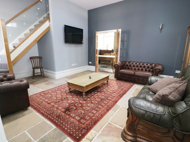 A living room with leather sofas a wooden coffee table a red patterned rug a wall mounted TV and a wooden chair at No 1 Church Cottages in Llanelli