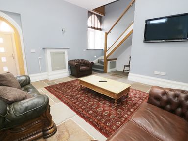 A living room with sofas a wooden coffee table a red patterned rug stairs and a wall-mounted television at No 1 Church Cottages in Llanelli