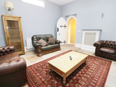 A living room with leather armchairs a wooden cabinet a coffee table and a red patterned rug at No 1 Church Cottages Llanelli