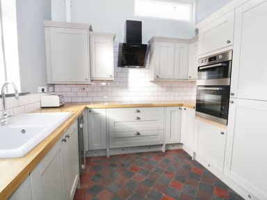 A kitchen with white cabinets wooden countertops a white sink a black cooker hood and a double oven at No 1 Church Cottages in Llanelli