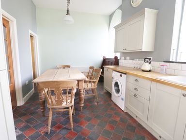 A kitchen with a wooden dining table and chairs washing machine and countertop with kettle and glasses at No 1 Church Cottages in Llanelli