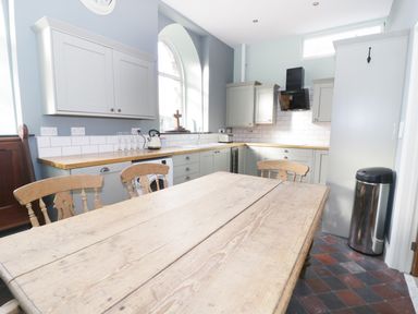 A kitchen with wooden table and chairs wooden countertops and gray cabinets at No 1 Church Cottages in Llanelli