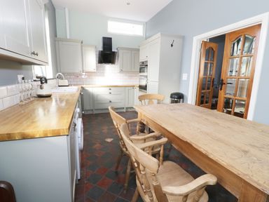 A kitchen with wooden table and chairs countertops cabinets oven and glass doors at No 1 Church Cottages in Llanelli