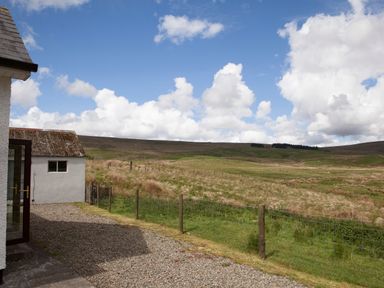 A gravel path next to a white building with a grassy field and hills under a partly cloudy sky at Shepherds Retreat in Gortin