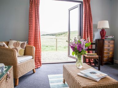 A living room with wicker furniture a vase with flowers books and an open door showing outdoor landscape at Shepherds Retreat in Gortin