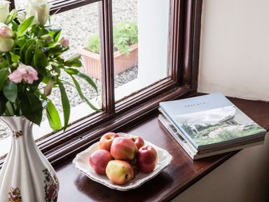 A windowsill with a vase of flowers apples on a plate and books at Shepherds Retreat in Gortin