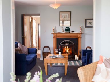 A living room with a lit fireplace two blue sofas a wooden table with wine and glasses at Shepherds Retreat in Gortin