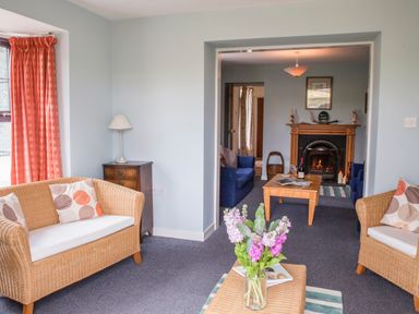 A seating area with wicker chairs and cushions a lamp on a wooden side table and a fireplace in the background at Shepherds Retreat in Gortin