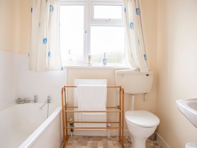 A bathroom with a bathtub a toilet a wooden towel rack with a towel and a window with curtains at Shepherds Retreat in Gortin