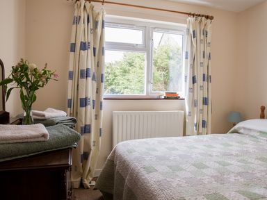 A bedroom with a bed covered in a patchwork quilt next to a window with curtains and a dresser with towels and flowers at Shepherds' Retreat in Gortin