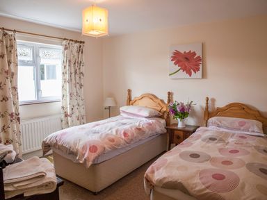 A bedroom with two single beds wooden headboards bedside table with flowers window with floral curtains at Shepherds Retreat in Gortin