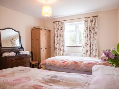 A bedroom with two single beds a wooden wardrobe a dresser with mirror and folded towels and floral curtains at Shepherds Retreat in Gortin