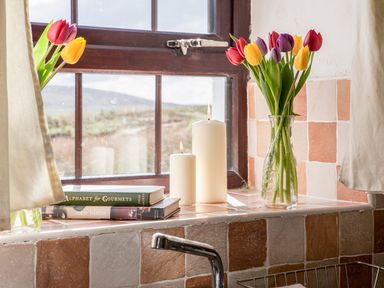 A kitchen window with two vases of tulips candles and cookbooks on the windowsill at Shepherds Retreat in Gortin