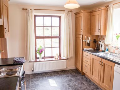 A kitchen with wooden cabinets a stove a black countertop and a window with curtains at Shepherds Retreat in Gortin