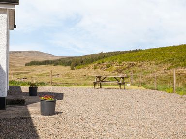 A gravel patio with two black plant pots and a wooden picnic table in a rural setting at Shepherds Retreat in Gortin