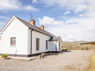 A white house with two chimneys and potted plants on a gravel driveway with picnic tables in a rural setting at Shepherds Retreat in Gortin