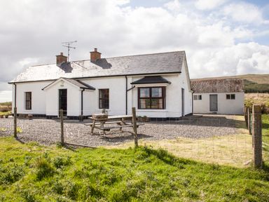 A white house with two chimneys a small porch and a wooden picnic table in front at Shepherds Retreat in Gortin