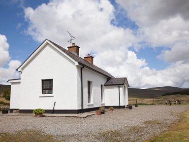 A white house with two chimneys and potted plants on a gravel driveway with hills in the background at Shepherds Retreat in Gortin