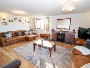A living room with brown leather sofas a wooden coffee table a rug a TV and a fireplace at Green Hills Farm in Ulverston