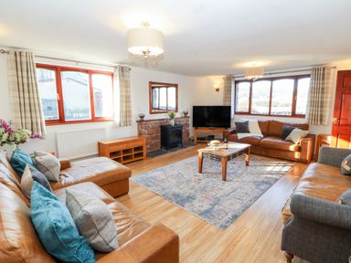 A living room with brown leather sofas a wooden coffee table a television and windows with checkered curtains at Green Hills Farm in Ulverston