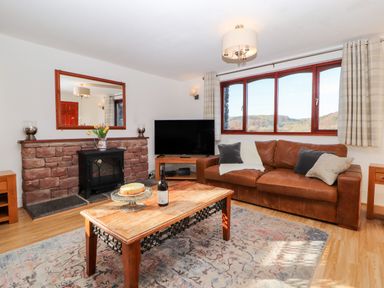 A living room with a brown leather sofa a wooden coffee table with cake and wine a stone fireplace and a large window with curtains at Green Hills Farm in Ulverston
