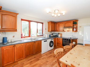 A kitchen with wooden cabinets a double sink washing machine oven and a wooden dining table with chairs at Green Hills Farm in Ulverston