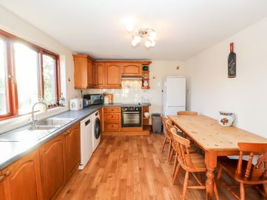 A kitchen with wooden cabinets a dining table with chairs a white refrigerator and large windows at Green Hills Farm in Ulverston