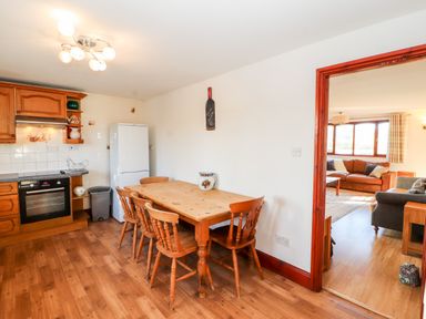 A kitchen with wooden table and chairs and a view into a living room at Green Hills Farm in Ulverston