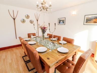 A dining room with a wooden table set with plates and glasses surrounded by brown chairs and wall decor at Green Hills Farm in Ulverston