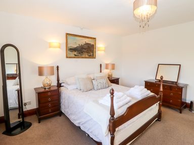A bedroom with a wooden bed frame white bedding a dresser with a mirror two bedside tables with lamps and a floor mirror at Green Hills Farm in Ulverston