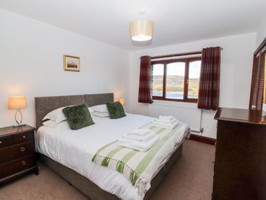 A bedroom with a double bed green cushions bedside tables with lamps a window with curtains and a dresser at Green Hills Farm in Ulverston